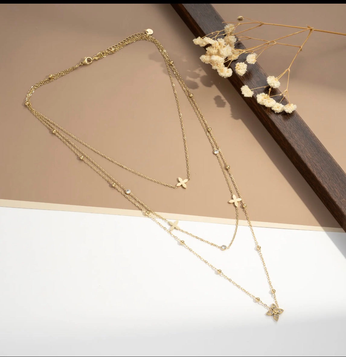 Collier multi-rangs doré avec fleurs à 4 pétales et perles sur fond beige