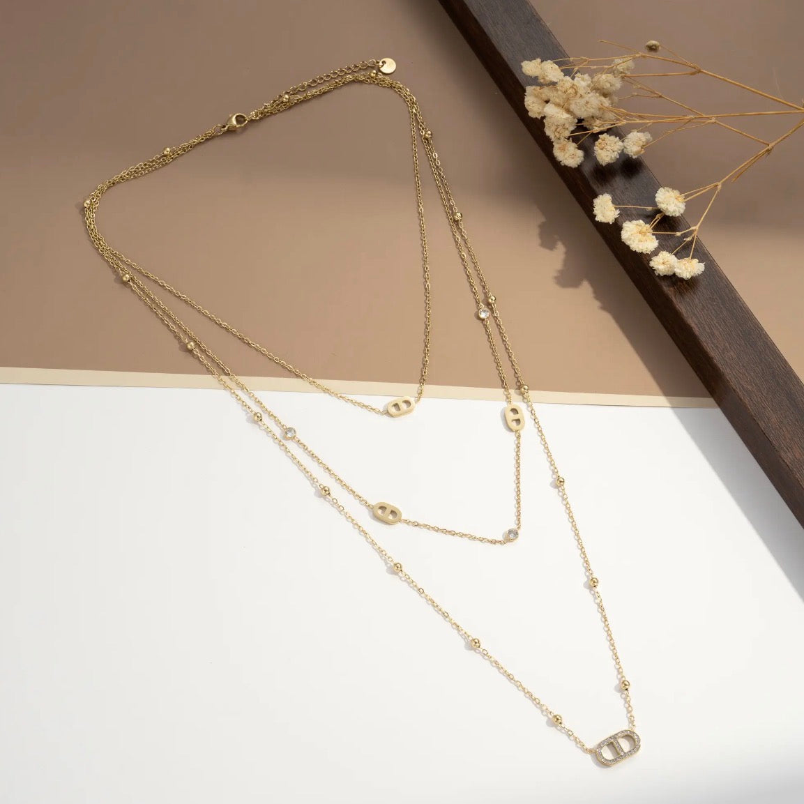 Collier multi-rangs doré avec maillons marins et zircons sur fond beige