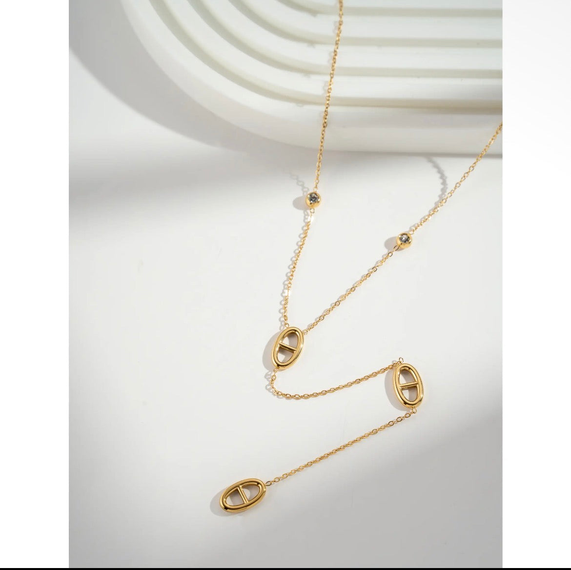 Collier lariat doré avec maillons marins ouverts et zircons sur fond blanc